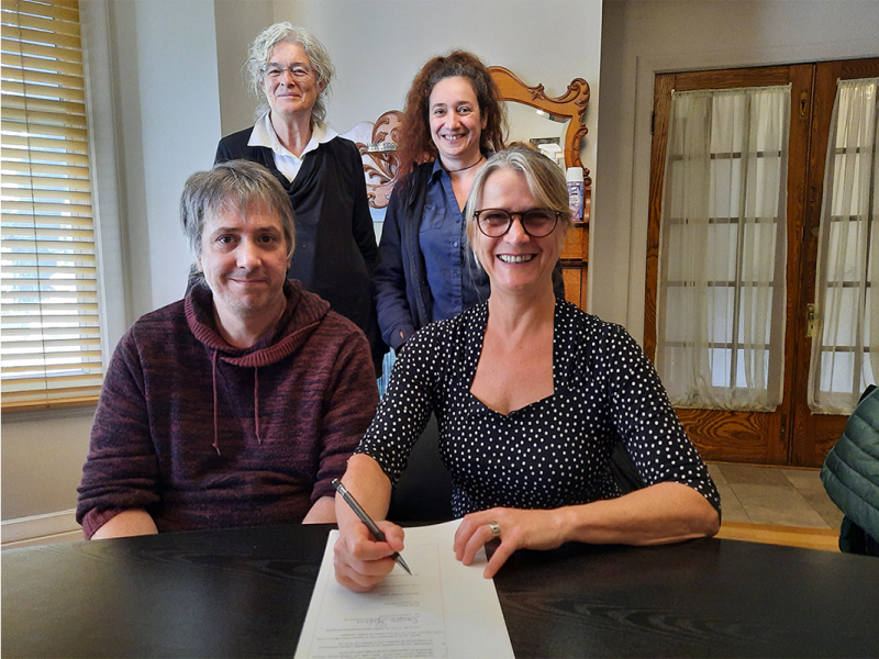 Line St. Amour, executive director of Plein Milieu, signs ownership papers for the organization’s newly purchased building while seated next to François Lefebvre, who’s father owned said property for many years. Board members Isabelle Raffestin (right) and Linda Roy (left) look on.