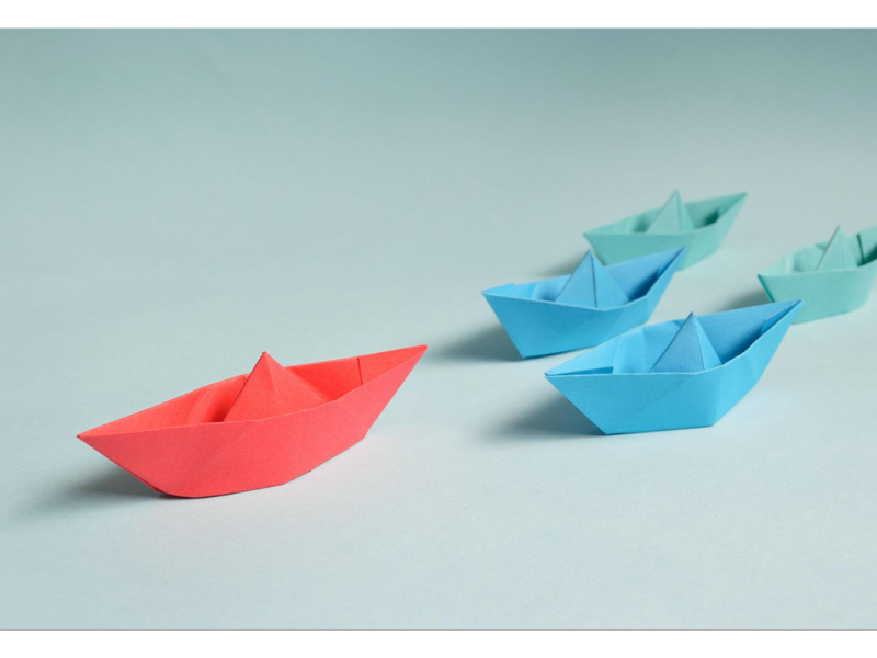3 paper boats. One red ahead of 2 blue boats.