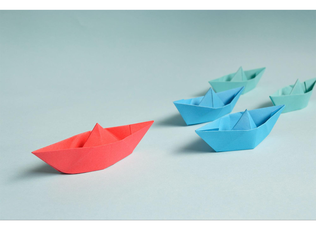 3 paper boats. One red ahead of 2 blue boats.