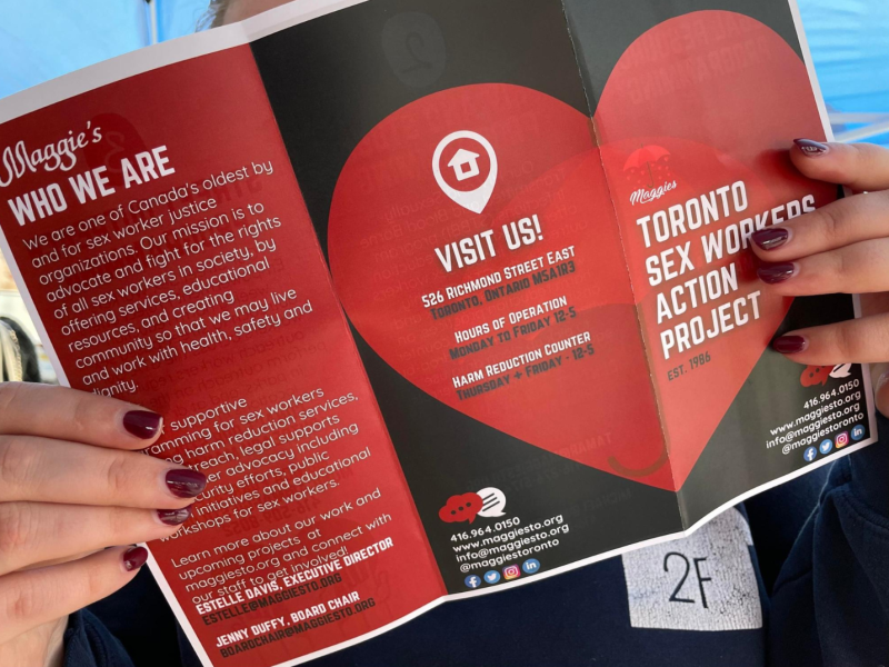 Women's hand holding a Maggie’s Toronto flyer relating to sex work
