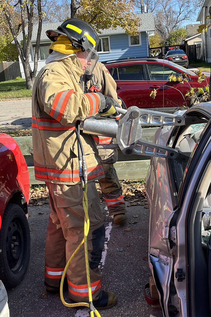 Young man uses a hydraulic tool to pry open a car door.