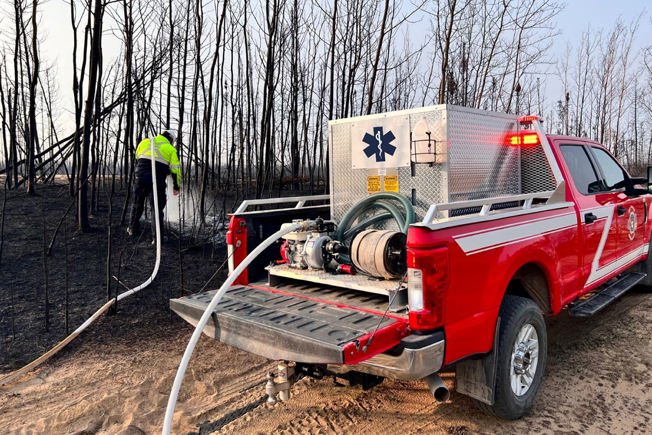 A pickup truck with a water tank and hose sits next to burnt trees.