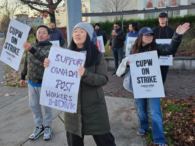 Canada Post workers wearing parkas hold signs reading "on strike" while on strike.