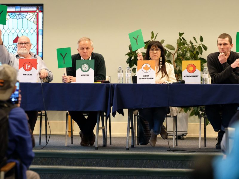 Ian MacIntyre of the Liberal Party, Gerry Gervais of the Green Party, Leah Gazan of the NDP and Cam Scott of the Communist Party take part in an election debate about accessibility at Winnipeg’s First Unitarian Universalist Church, while sitting behind a long table holding up green signs with the letter "Y" on them, on April 8, 2025