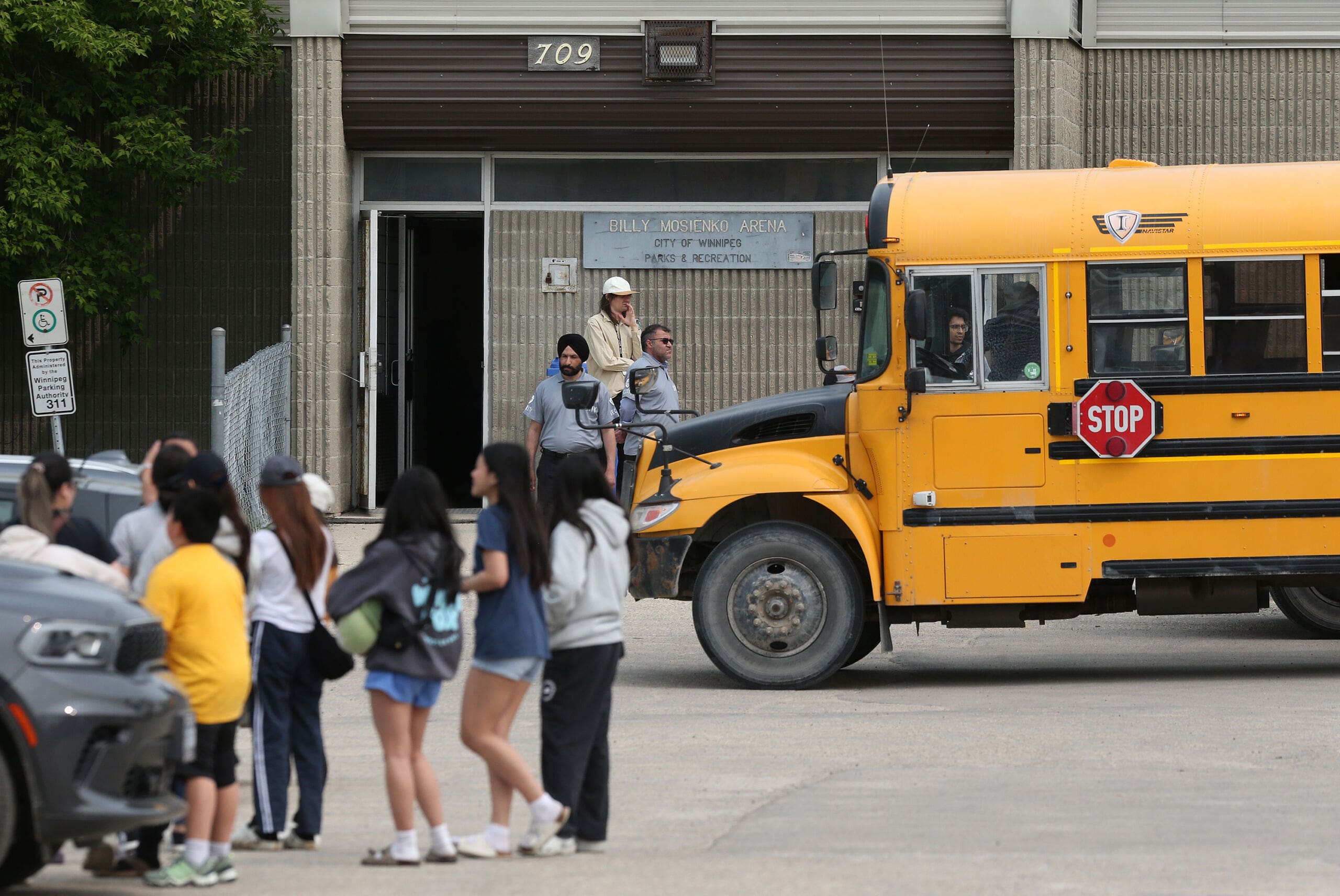 Wildfire evacuees at a Red Cross centre in Winnipeg. Youth are arriving by school bus at a brick arena.