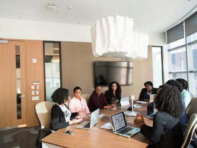 Women of colour sit around a wooden boardroom table.