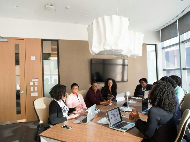 Women of colour sit around a wooden boardroom table.
