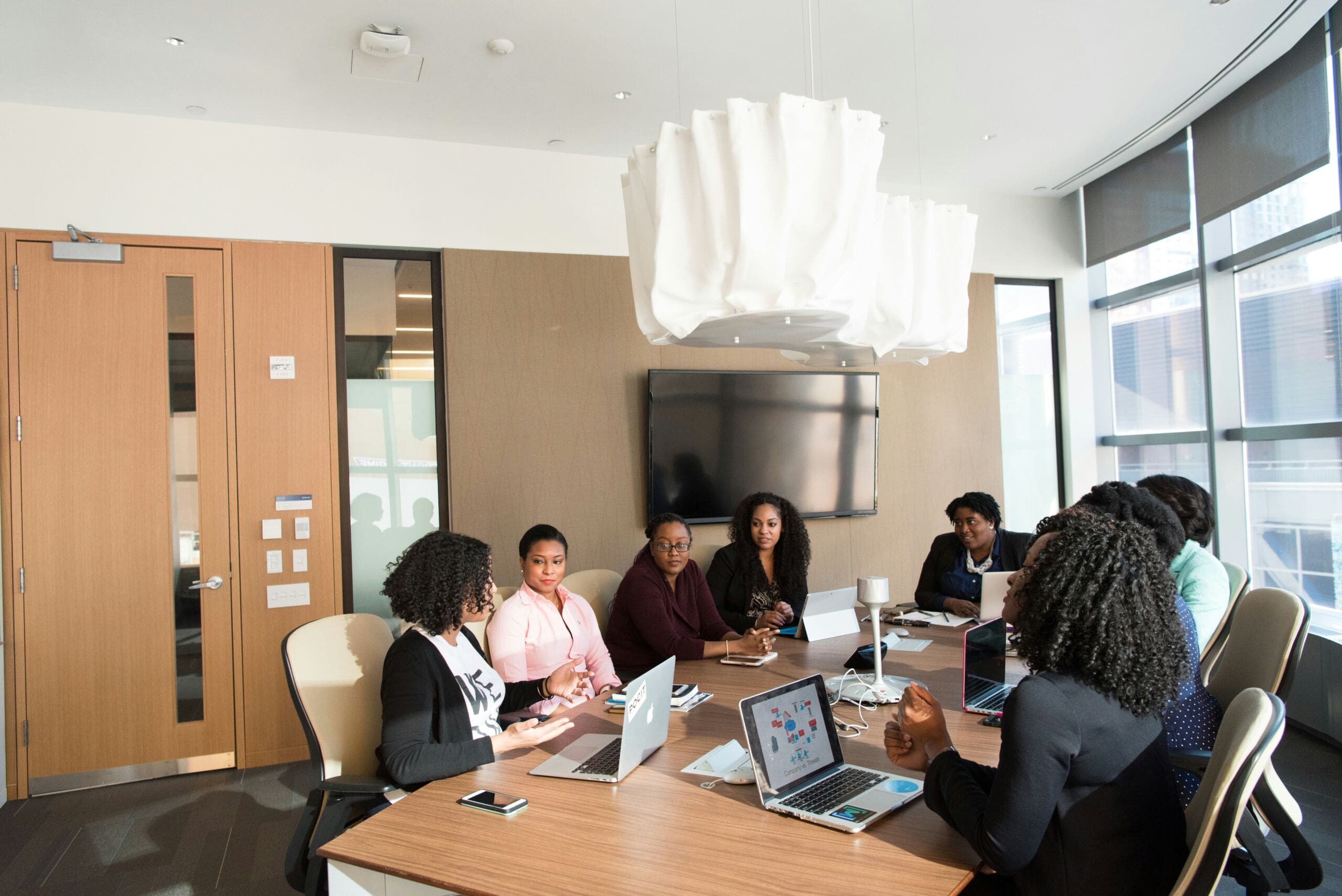 Women of colour sit around a wooden boardroom table.